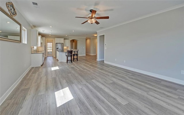 unfurnished living room with light wood finished floors, visible vents, arched walkways, baseboards, and ornamental molding