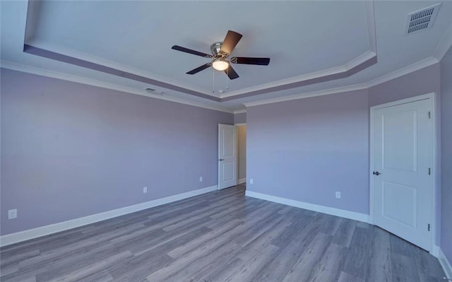 unfurnished room featuring a tray ceiling, visible vents, ceiling fan, wood finished floors, and baseboards