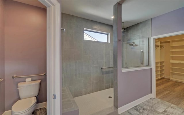 bathroom with a walk in shower, toilet, wood finished floors, baseboards, and a spacious closet