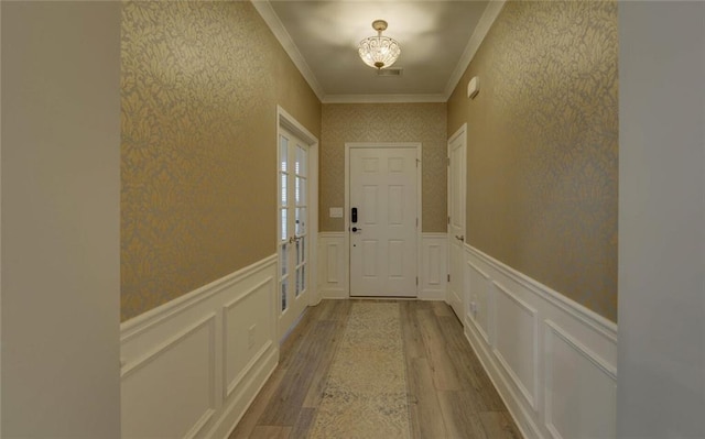 doorway to outside featuring light wood-style floors, a decorative wall, crown molding, and wainscoting