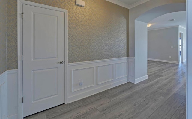 unfurnished room featuring arched walkways, a wainscoted wall, crown molding, and wallpapered walls