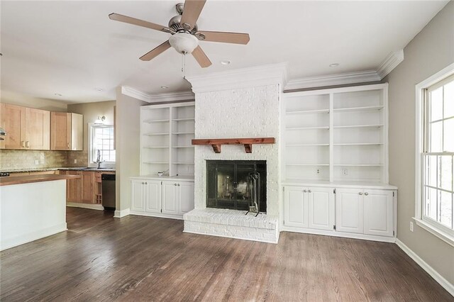 unfurnished living room with ceiling fan, a fireplace, sink, ornamental molding, and dark hardwood / wood-style flooring