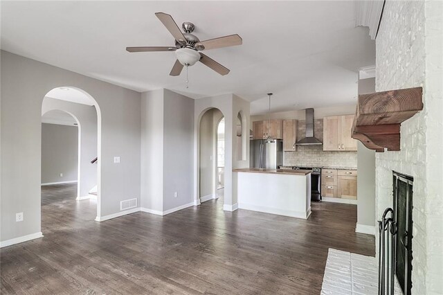 kitchen with appliances with stainless steel finishes, wall chimney exhaust hood, decorative light fixtures, decorative backsplash, and a brick fireplace