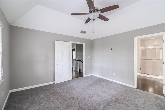 unfurnished bedroom with lofted ceiling, ensuite bath, multiple windows, dark colored carpet, and ceiling fan