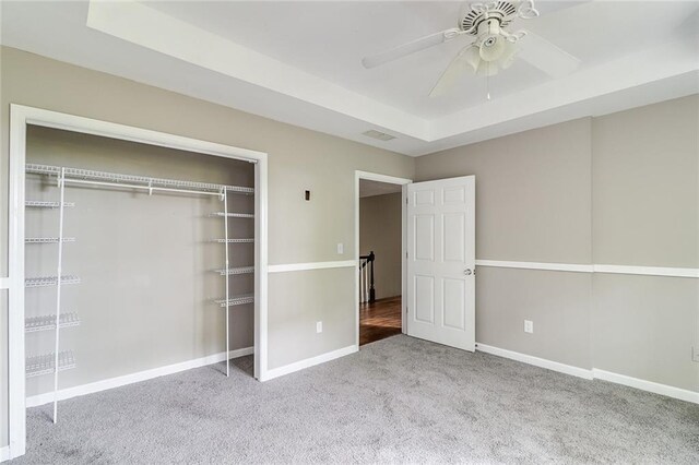 unfurnished bedroom featuring ceiling fan, a closet, light carpet, and a raised ceiling