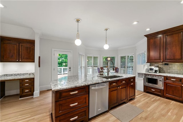 kitchen featuring a kitchen island with sink, light wood-type flooring, decorative light fixtures, stainless steel appliances, and sink