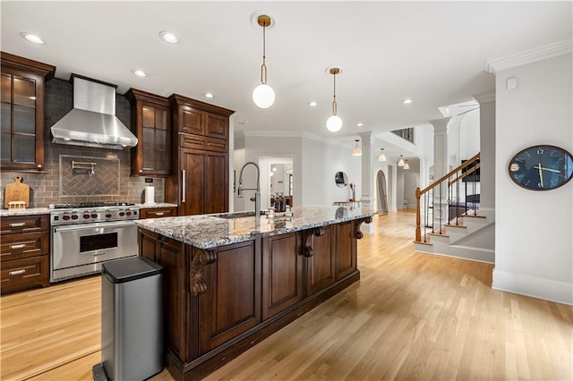 kitchen featuring light hardwood / wood-style flooring, high end appliances, sink, ornate columns, and wall chimney exhaust hood