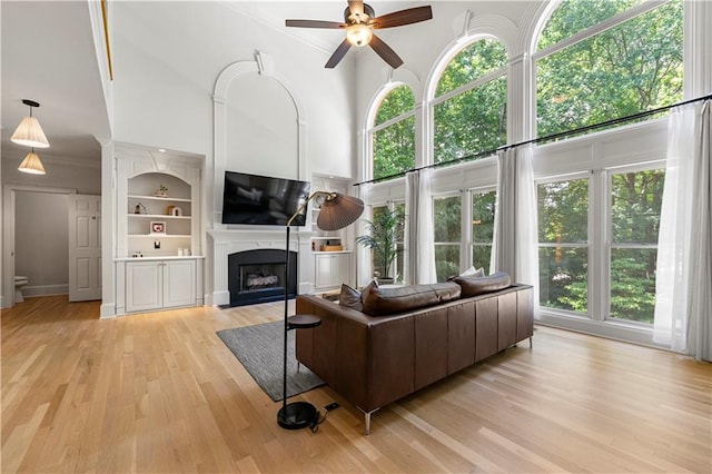 living room with a high ceiling, ornamental molding, built in features, light hardwood / wood-style flooring, and ceiling fan