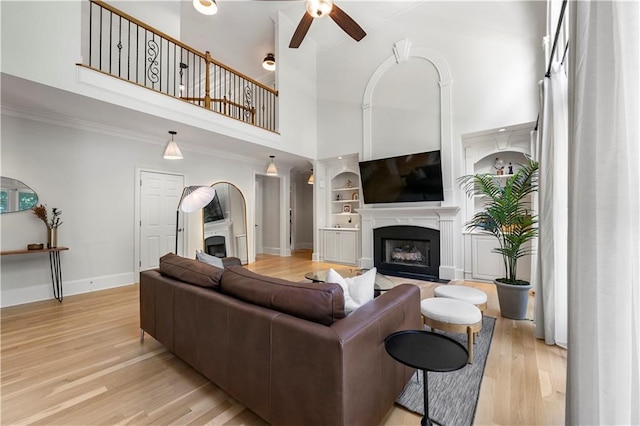 living room with a towering ceiling, light wood-type flooring, crown molding, and ceiling fan