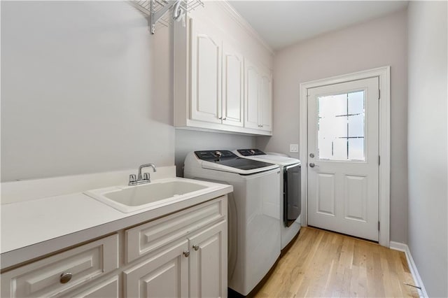 clothes washing area featuring cabinets, washer and clothes dryer, sink, and light hardwood / wood-style floors