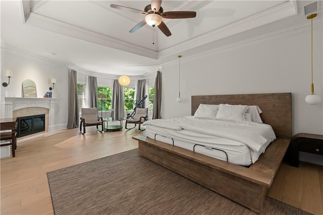 bedroom with ceiling fan, a raised ceiling, crown molding, and light hardwood / wood-style flooring