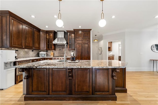 kitchen featuring a center island with sink, hanging light fixtures, wall chimney exhaust hood, and light hardwood / wood-style floors