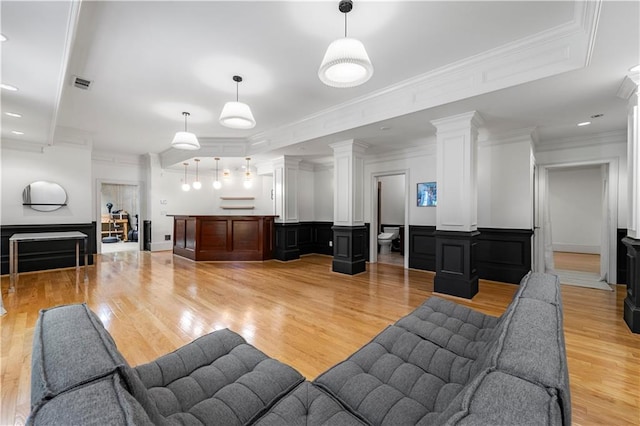 living room with a fireplace, crown molding, light wood-type flooring, and ornate columns