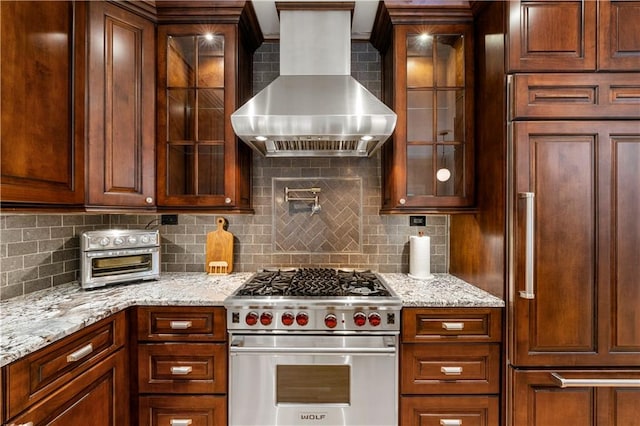 kitchen featuring high end appliances, light stone counters, backsplash, and wall chimney range hood