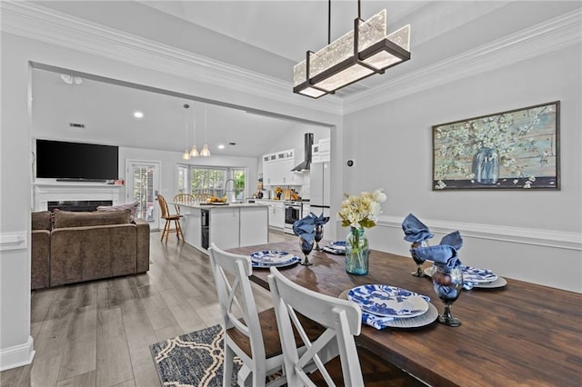 dining space featuring crown molding, lofted ceiling, sink, and light hardwood / wood-style flooring