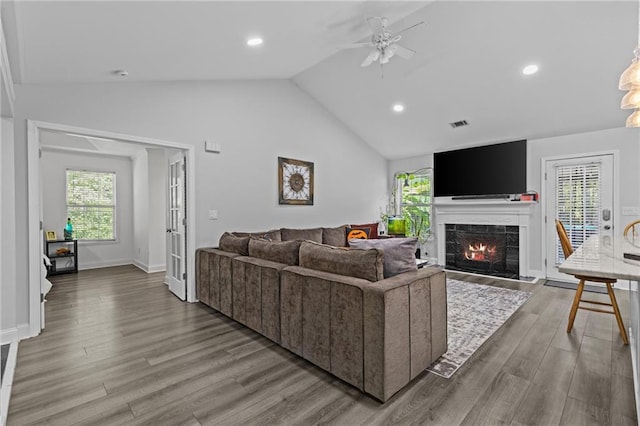 living room featuring ceiling fan, a tiled fireplace, vaulted ceiling, and light wood-type flooring