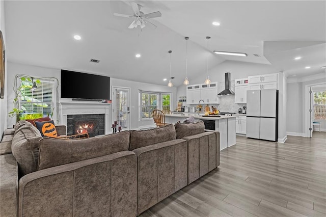 living room featuring a tile fireplace, lofted ceiling, sink, ceiling fan, and light hardwood / wood-style flooring