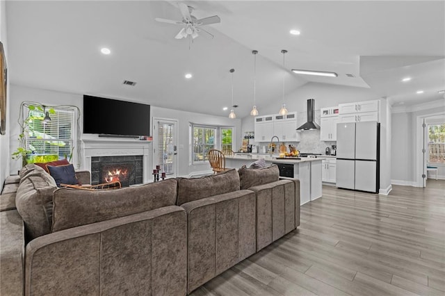 living room featuring lofted ceiling, sink, light hardwood / wood-style flooring, a tile fireplace, and ceiling fan