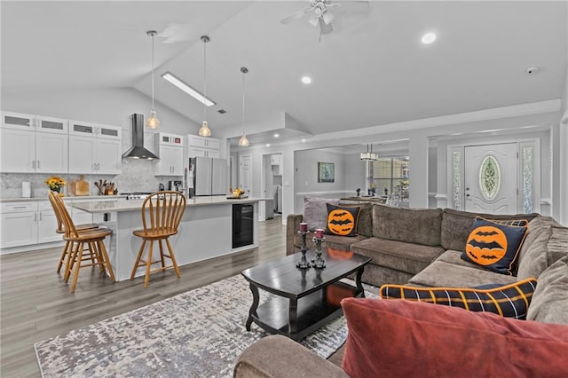 living room featuring ceiling fan, beverage cooler, high vaulted ceiling, and light hardwood / wood-style flooring