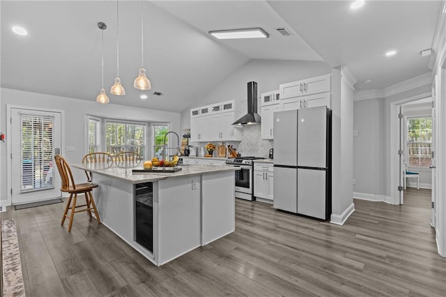 kitchen featuring stainless steel gas stove, white cabinetry, refrigerator, an island with sink, and wall chimney range hood