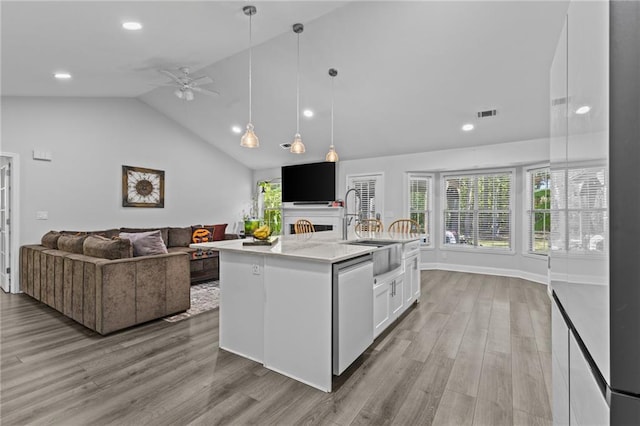 kitchen featuring pendant lighting, white cabinets, a kitchen island with sink, stainless steel dishwasher, and light wood-type flooring