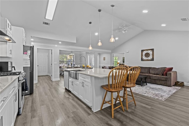 kitchen with a breakfast bar, hanging light fixtures, stainless steel appliances, white cabinets, and a center island with sink