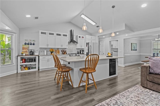 kitchen featuring wall chimney range hood, refrigerator, white cabinetry, a kitchen bar, and decorative light fixtures