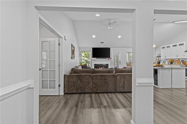 living room with ceiling fan, lofted ceiling, beverage cooler, and light hardwood / wood-style flooring