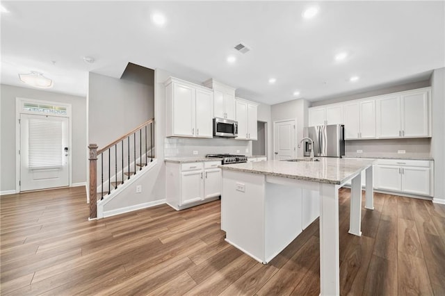 kitchen with a center island with sink, white cabinetry, stainless steel appliances, and light stone countertops