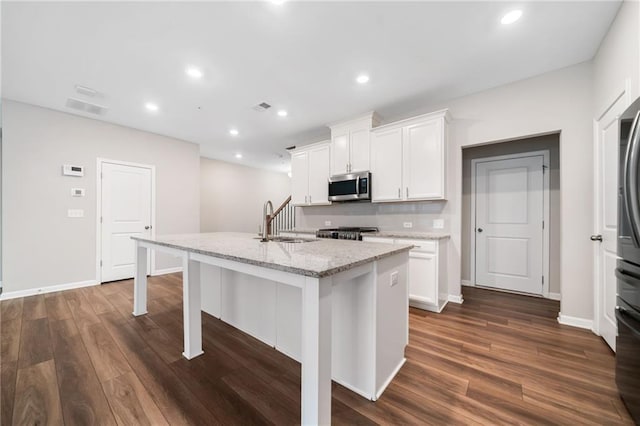 kitchen featuring a center island with sink, stainless steel appliances, light stone counters, sink, and white cabinetry