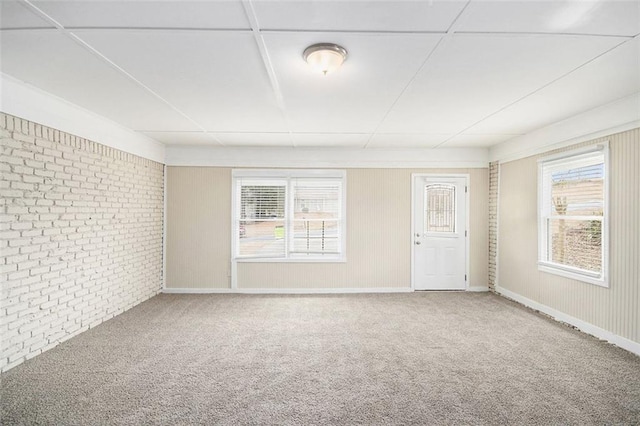 carpeted spare room with baseboards and brick wall