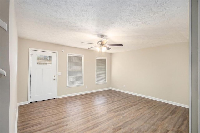 empty room with a ceiling fan, a textured ceiling, baseboards, and wood finished floors