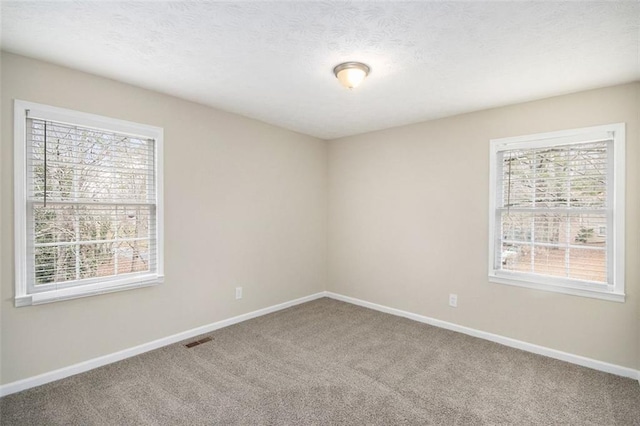 empty room featuring a wealth of natural light, baseboards, visible vents, and carpet