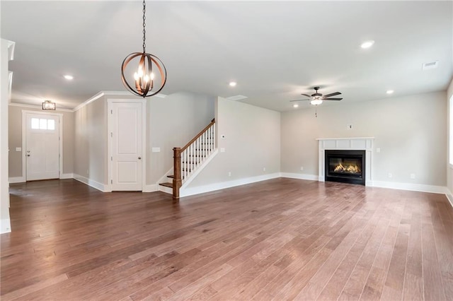 unfurnished living room featuring recessed lighting, wood finished floors, stairs, and ceiling fan with notable chandelier