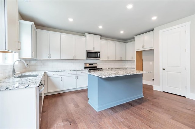 kitchen with light wood finished floors, light stone counters, stainless steel appliances, white cabinetry, and a sink