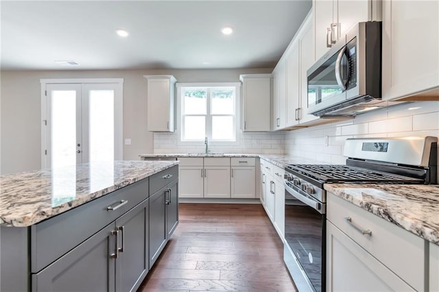 kitchen with gray cabinetry, wood finished floors, stainless steel appliances, decorative backsplash, and light stone countertops