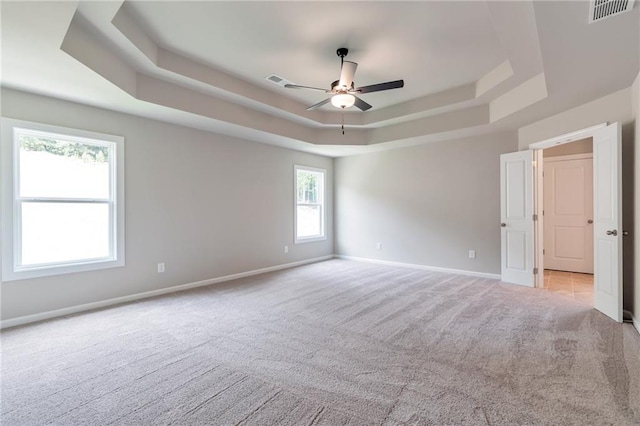 carpeted empty room featuring a tray ceiling, a ceiling fan, visible vents, and baseboards