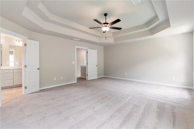 unfurnished bedroom with ensuite bath, a raised ceiling, baseboards, and light carpet