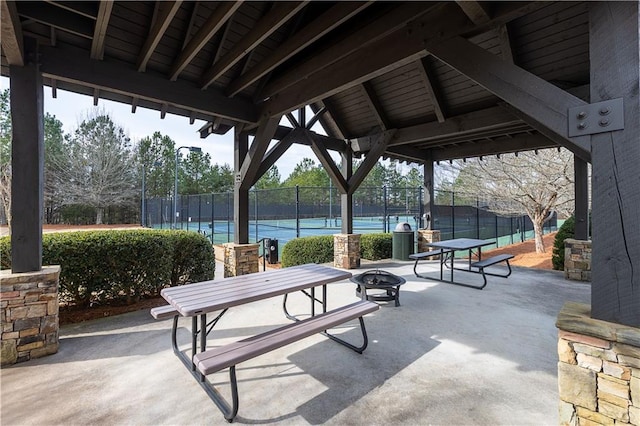 view of patio with a tennis court, fence, and an outdoor fire pit