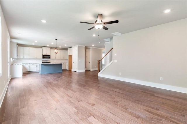 unfurnished living room featuring ceiling fan, recessed lighting, wood finished floors, and stairs