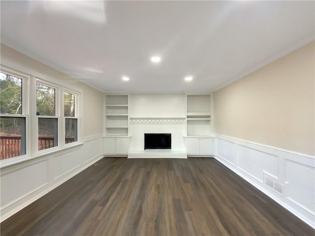 unfurnished living room featuring a large fireplace, built in features, and dark hardwood / wood-style floors