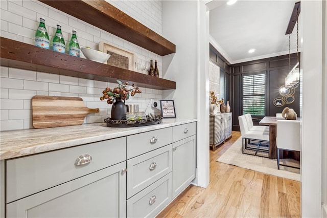 bar with decorative backsplash, crown molding, light hardwood / wood-style floors, and light stone counters