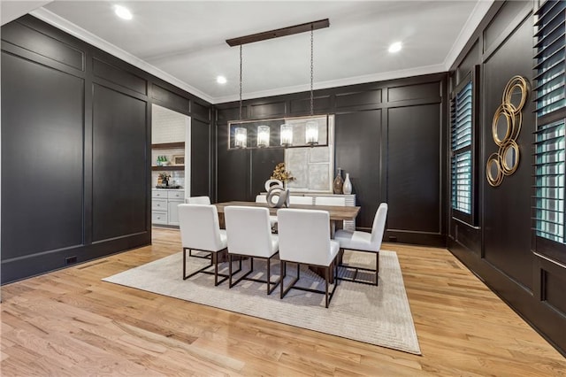 dining area featuring light wood-type flooring, ornamental molding, and a notable chandelier