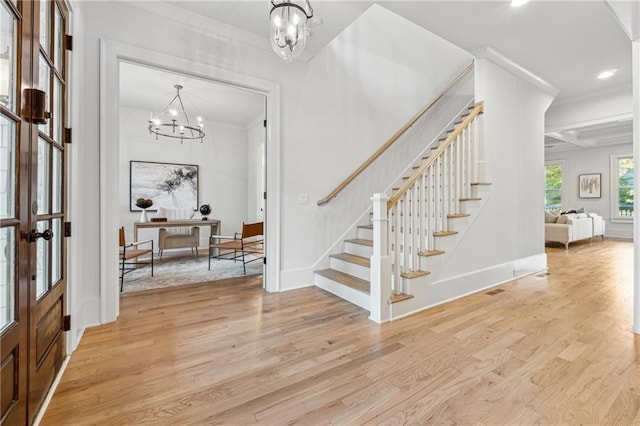 foyer entrance featuring french doors, crown molding, beam ceiling, a notable chandelier, and light hardwood / wood-style floors