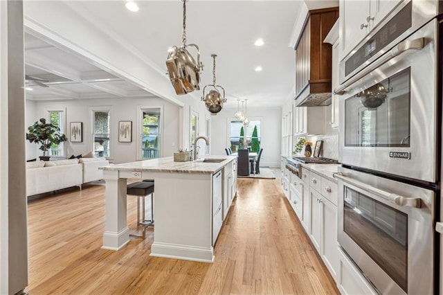 kitchen featuring a kitchen island with sink, coffered ceiling, light hardwood / wood-style floors, white cabinetry, and stainless steel appliances