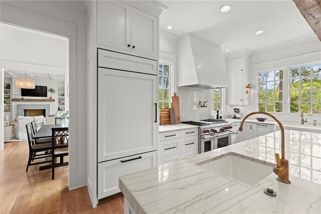 1141 Ragley Hall Rd NE, Brookhaven, GA 30319 - kitchen featuring range with two ovens, wall chimney range hood, white cabinetry, tasteful backsplash, and ornamental molding