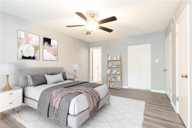 bedroom with light wood-style flooring, a closet, ceiling fan, and baseboards