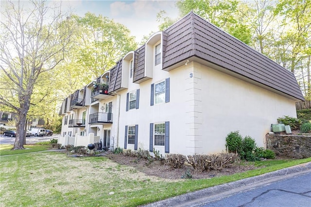 view of side of property featuring mansard roof, stucco siding, and a lawn