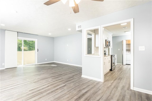 unfurnished living room featuring baseboards, light wood-style flooring, washer / dryer, visible vents, and ceiling fan