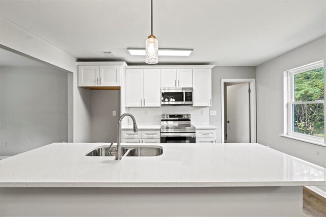 kitchen featuring an island with sink, stainless steel appliances, sink, pendant lighting, and white cabinetry